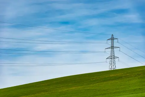 A lone power pylon on a green hill under a blue sky
