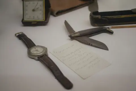 Wristwatch, pocket knife and a handwritten note laid out on a table