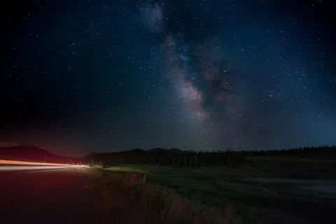 Lone empty road stretching into darkness under a dense Milky Way sky