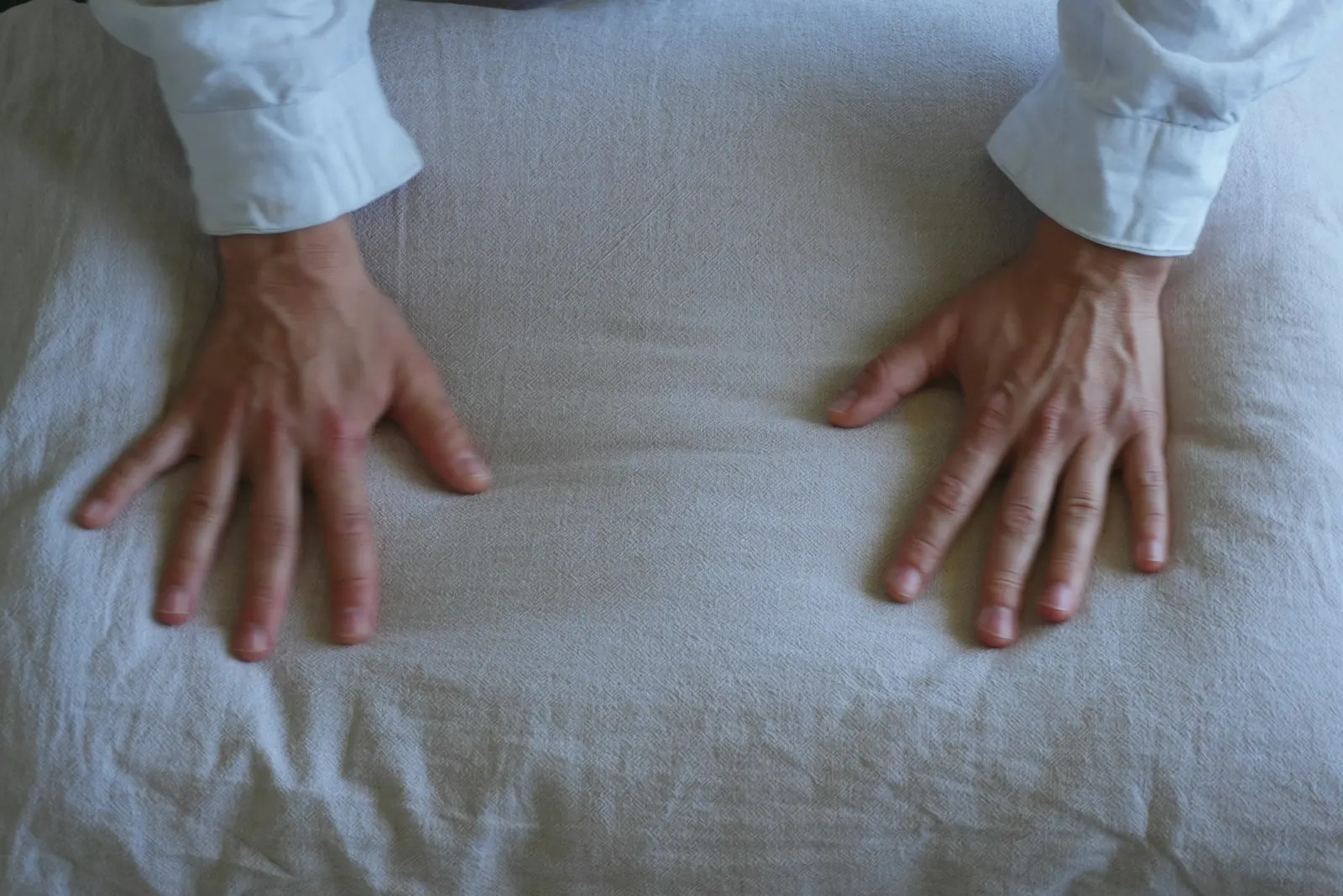 Two hands pressing flat on a soft linen pillow